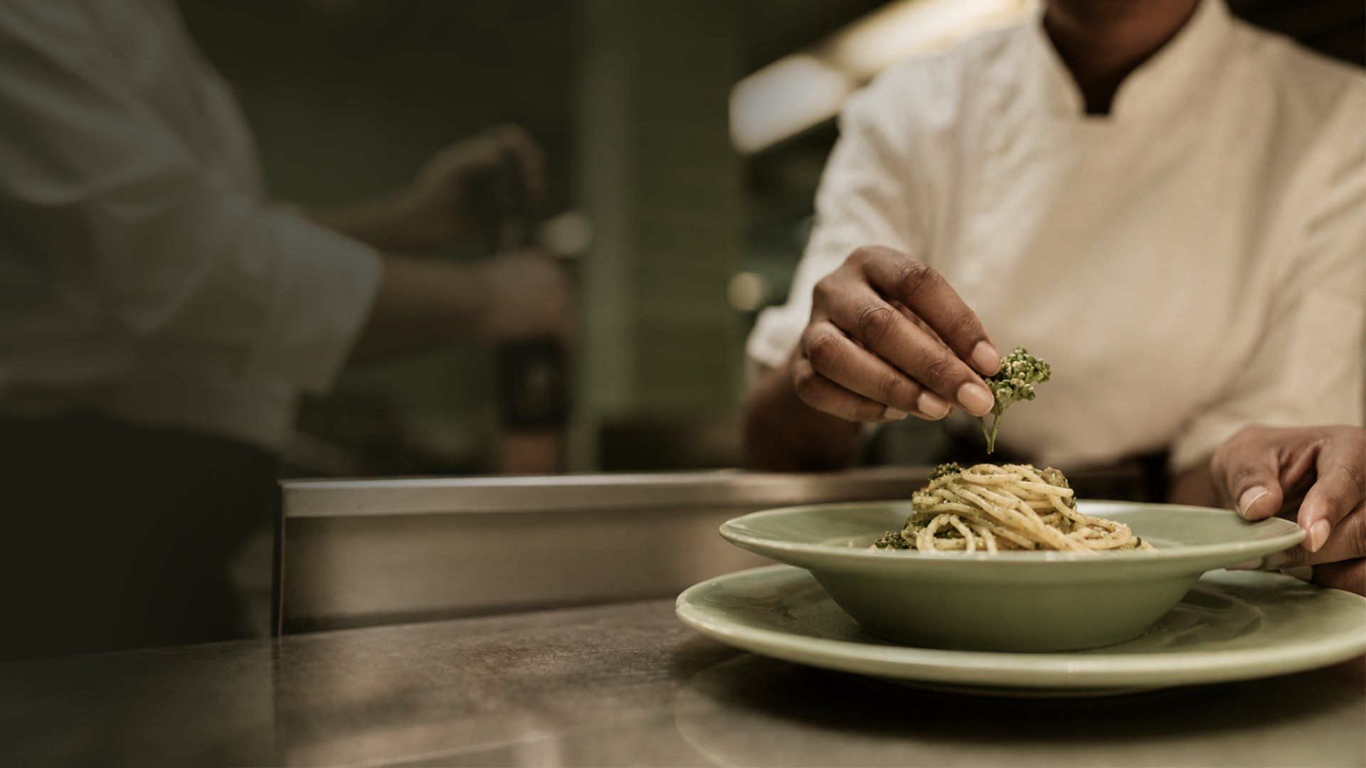 A chef plating pasta in a restaurant kitchen